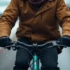 A man in a winter coat rides a bike, enjoying the chilly weather with a smile on his face.